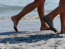 Des pieds qui marchent sur la plage, illustrant comment prendre soins des pieds après les vacances.