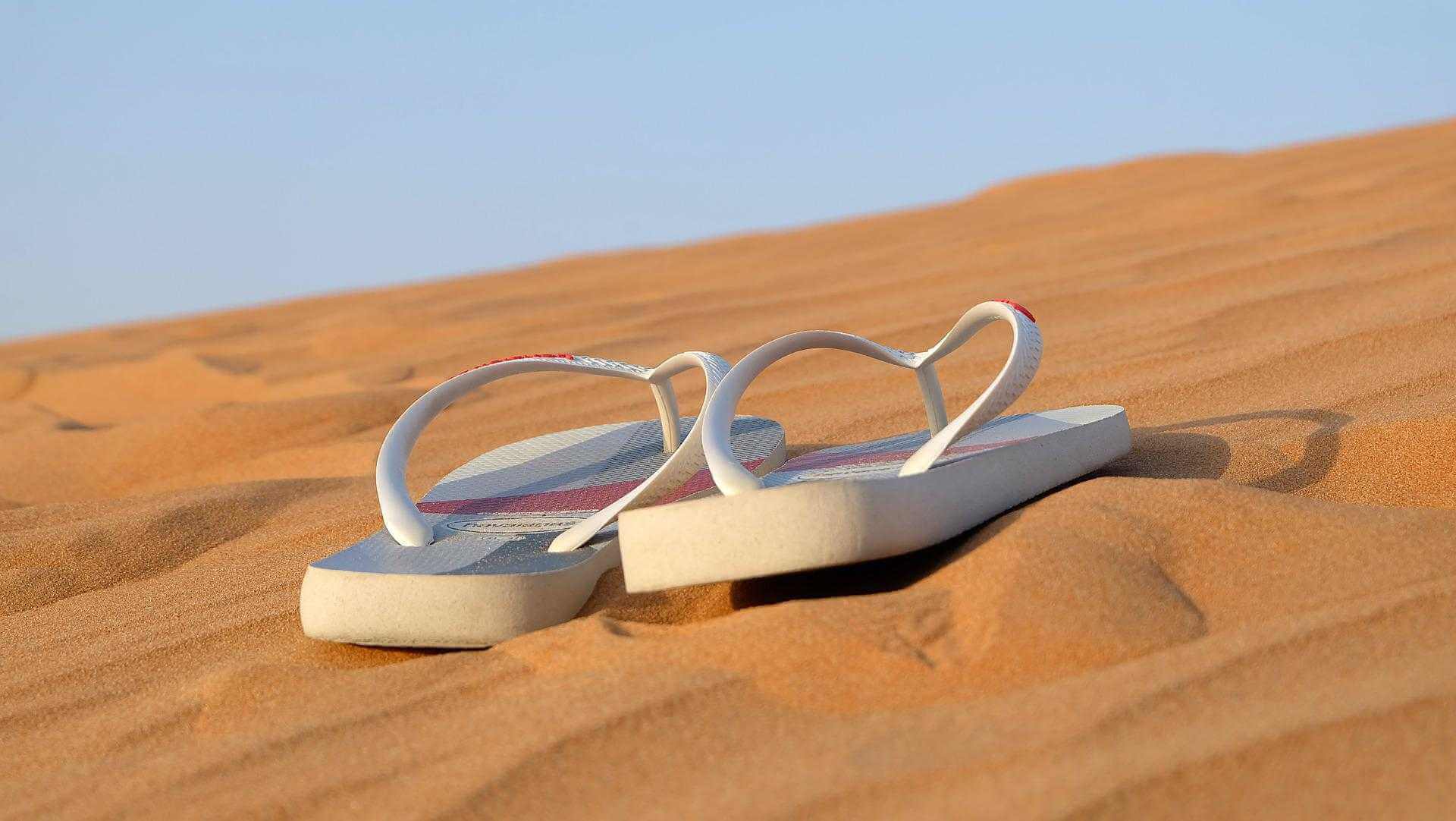 Paire de tongs blanches posées sur du sable fin