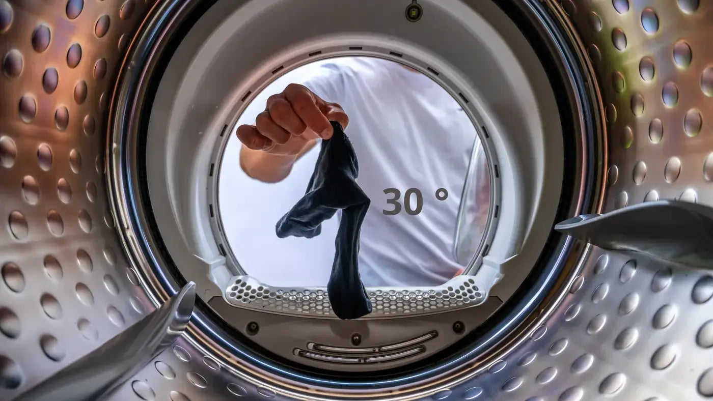 Un homme place une chaussette dans un tambour de machine à laver pour un lavage à 30°