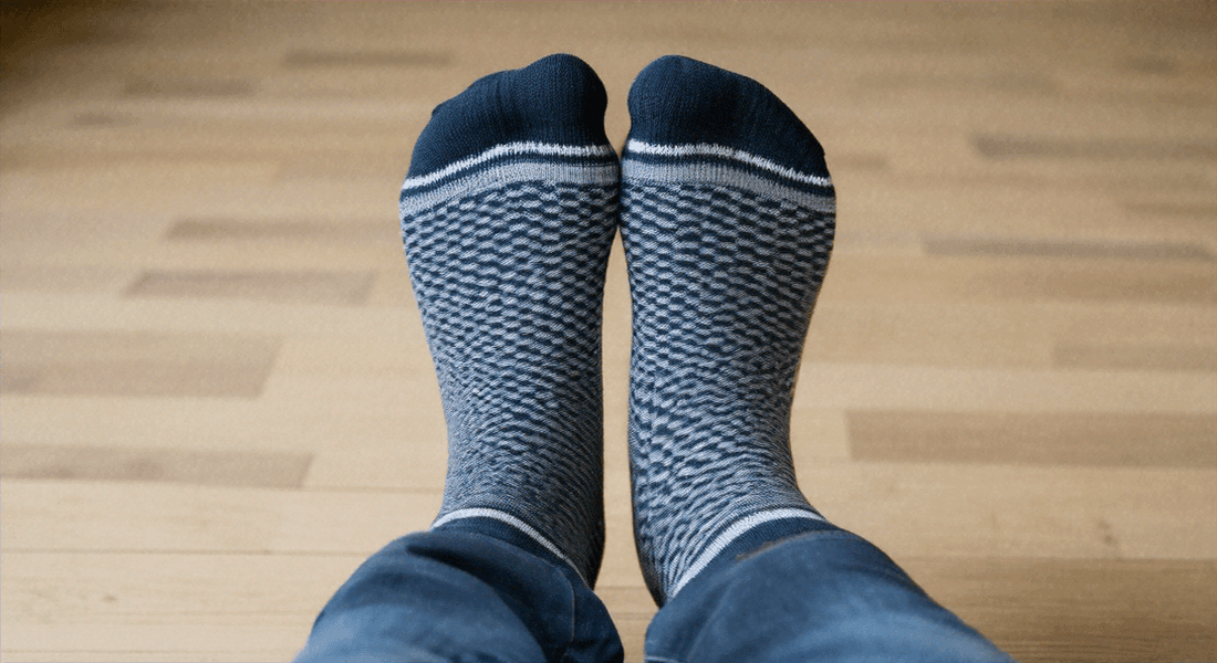 Deux pieds dans des chaussettes avec un motif géométrique, mettant le pied dans la chaussette.
