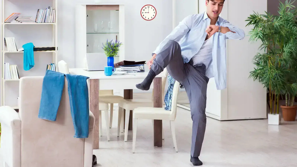 Jeune homme se dépêchant d'enfiler ses chaussettes dans un salon moderne, illustrant la gestion du temps le matin.