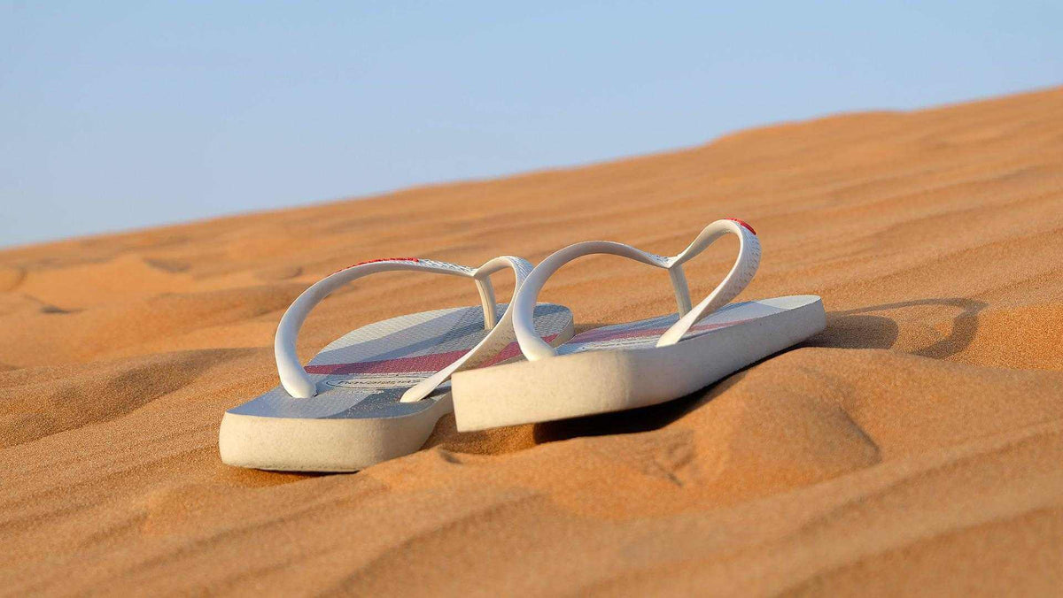 Paire de tongs blanches posées sur du sable fin