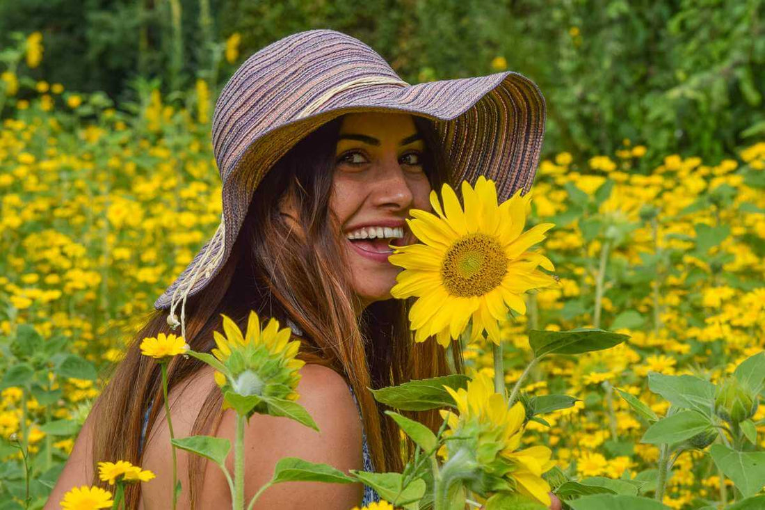 Femme avec un chapeau qui sourit dans un champs de tournesols