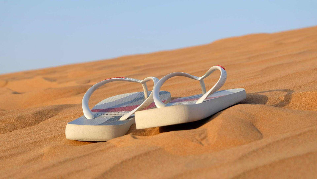 Paire de tongs blanches posées sur du sable fin