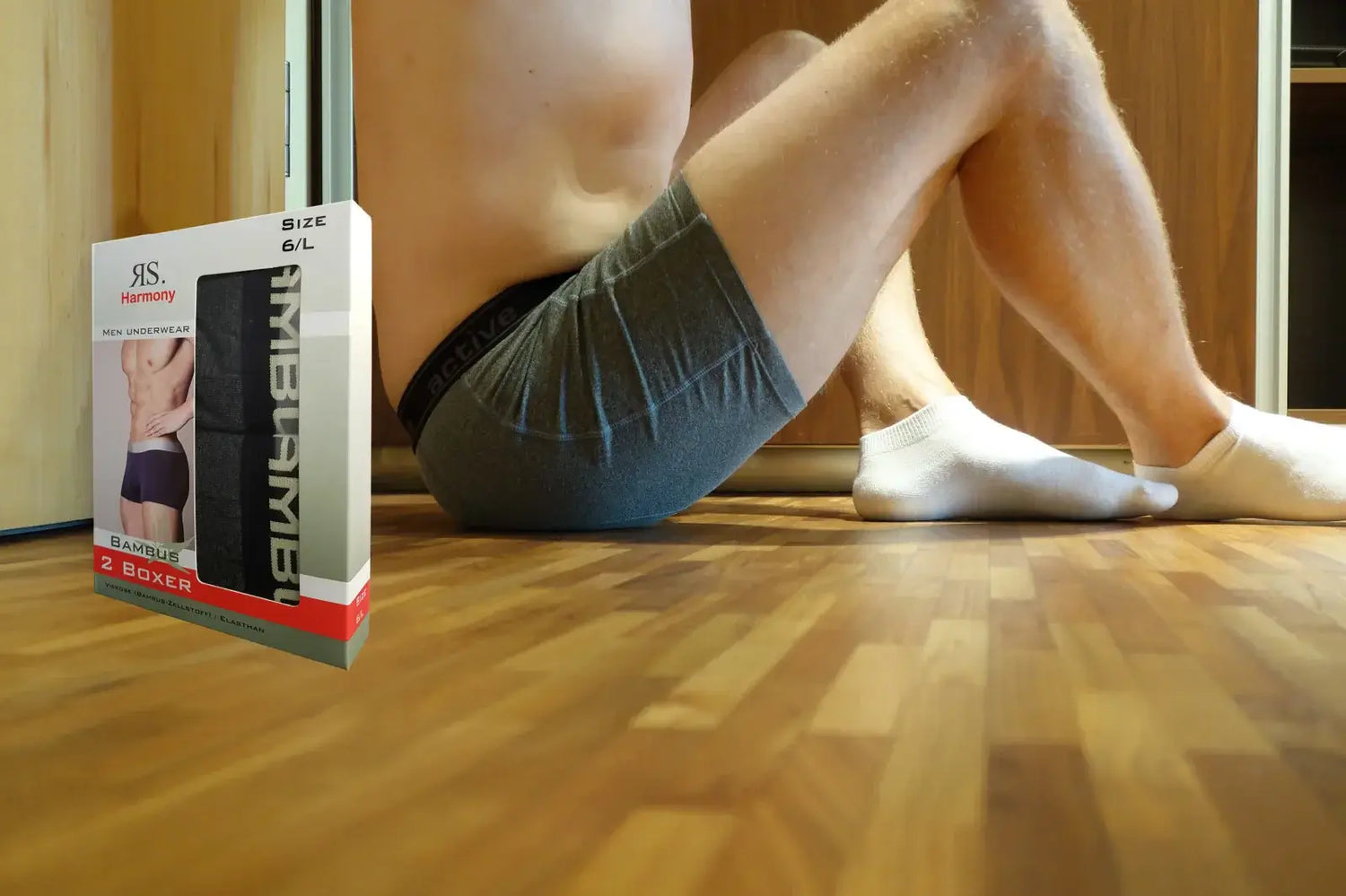 Un homme en boxer bambou assis sur le parquet avec des mini-socquettes bambou aux pieds