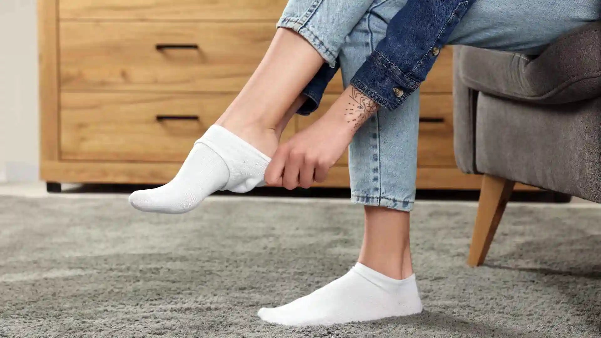 Femme assise dans un fauteuil  enfile sur son pied droit une paire de mini-socquettes blanches.